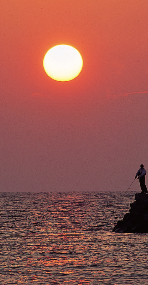 玄界灘の夕日。岩場で釣り糸を垂れる人の姿も。/